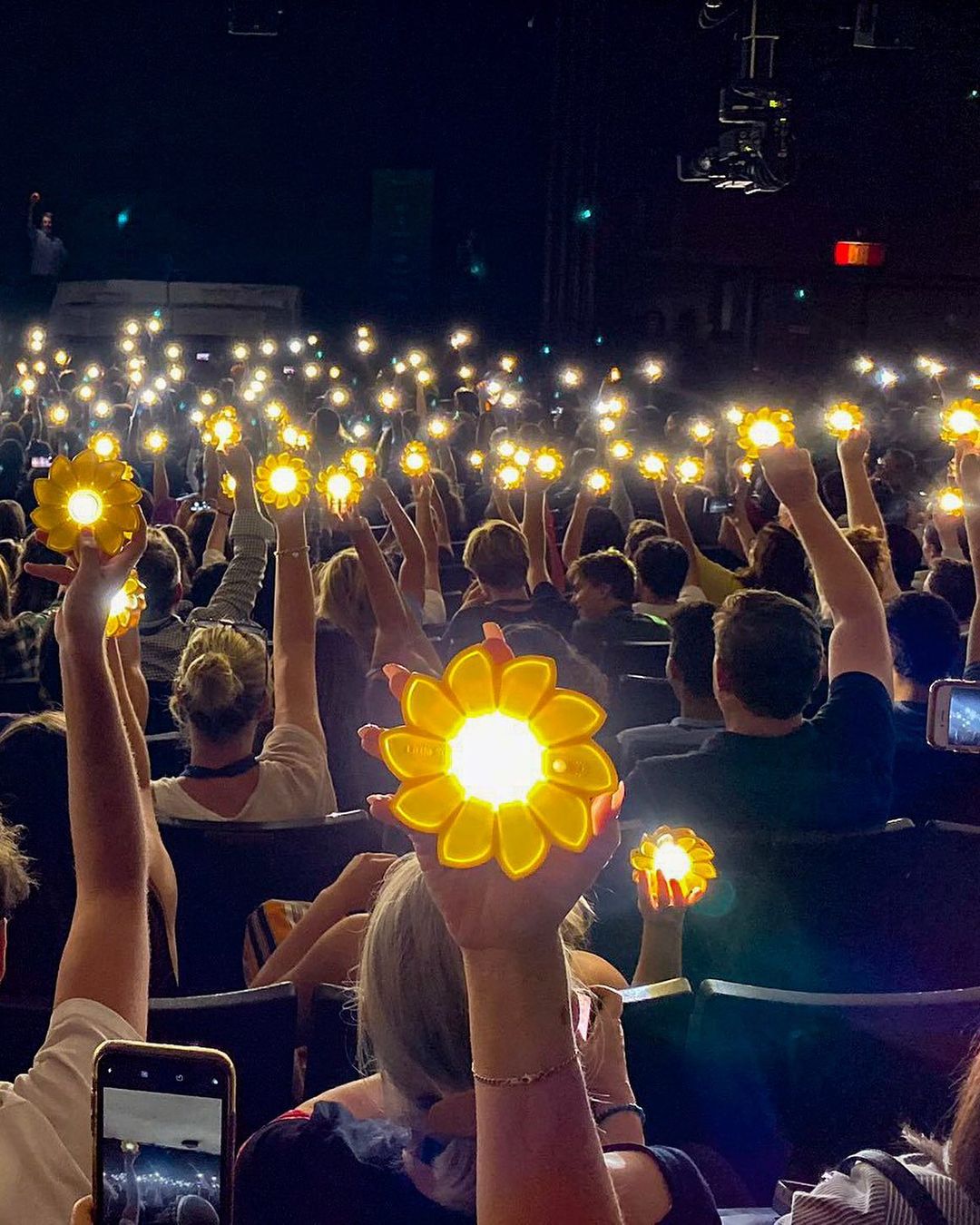 Many people holding glowing sunflower like devices in their hands